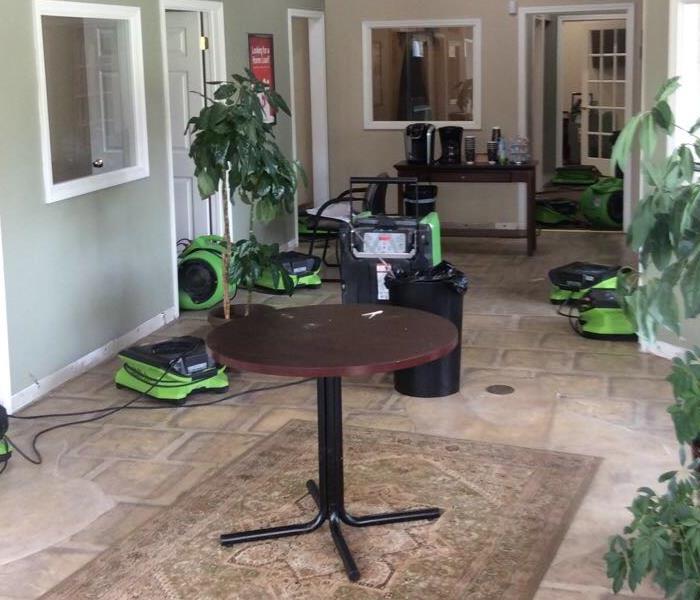 Office with vinyl flooring drying with SERVPRO drying equipment, plans, rug and tables throughout the room.  