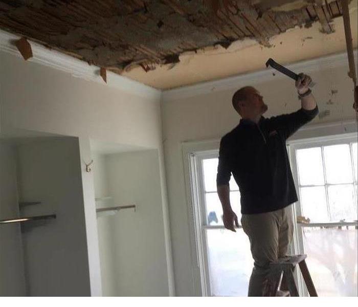 A man on a step ladder demolishing a damaged ceiling 