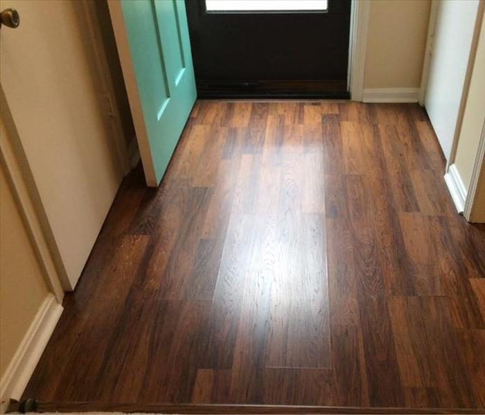 Dark Hardwood floor with wide planks in a foyer bear a green front door.  Sewage damage causing the floor to buckle