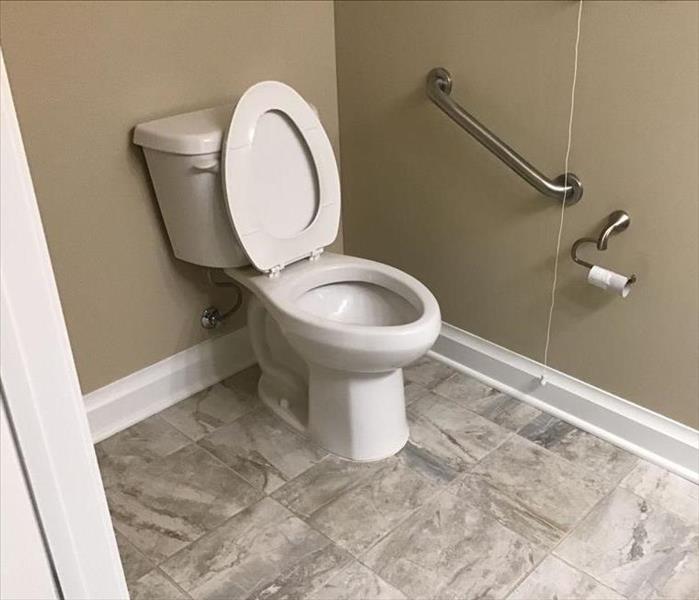 Bathroom with grey square tile.  New white toilet with seat raised.  White baseboard around room.