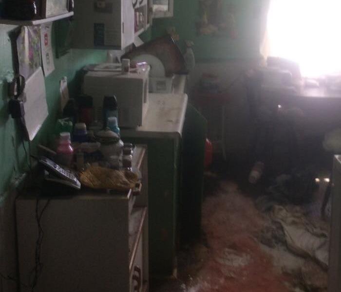 Image of a kitchen in total disarray following a flood.  The floor is covered with debris and stuff is literally everywhere  