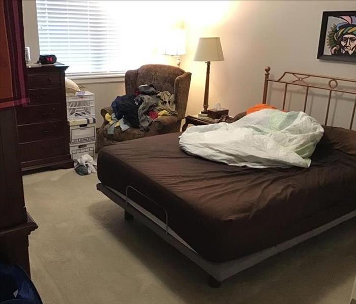 Bedroom with a chair, bed, chest of drawers and carpet flooring.  The bed has a brown sheet and mattress pad on top.  