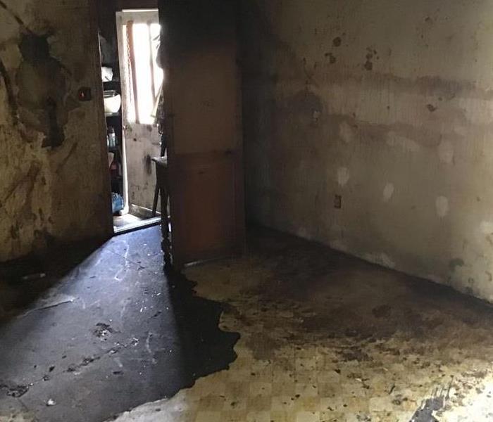 Fire damaged room with soot damage to walls and flooring.  The room is cleared out of contents.