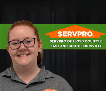woman with red hair smiling at the camera with a SERVPRO logo on the wall